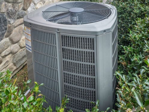 An AC unit surrounded by bushes in a backyard